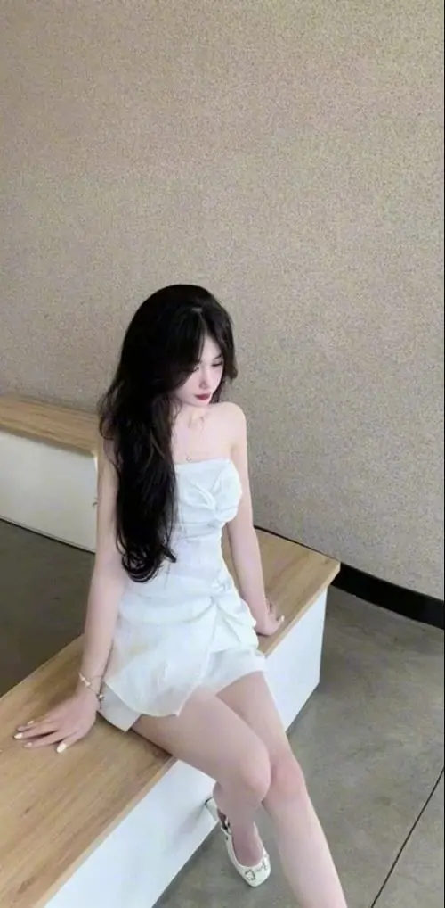 Góc tường tối giản ghi lại hình ảnh thiếu nữ mặc váy ngắn trắng, cô gái đứng nghiêng nhẹ, tóc dài phủ vai trông thanh thoát