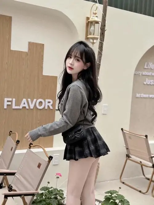 Tại quán cà phê, gái xinh mặc váy ngắn đen phối áo khoác tối màu, đứng nghiêng bên bảng hiệu với mái tóc dài