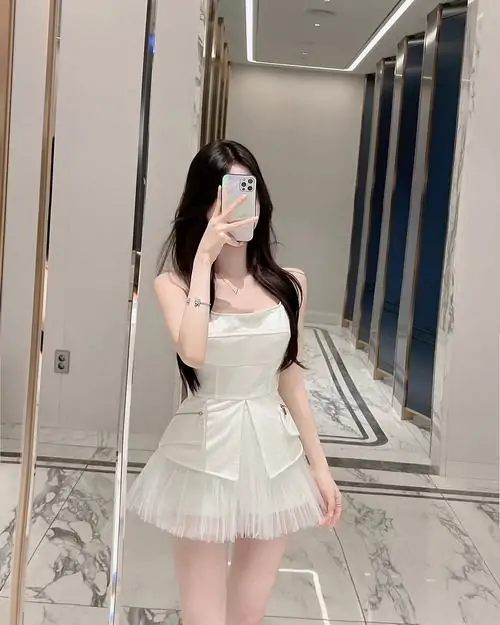 Tấm gương trong phòng ghi lại ảnh hot girl váy ngắn xếp ly, cô gái mặc áo kem và váy trắng tạo dáng che mặt