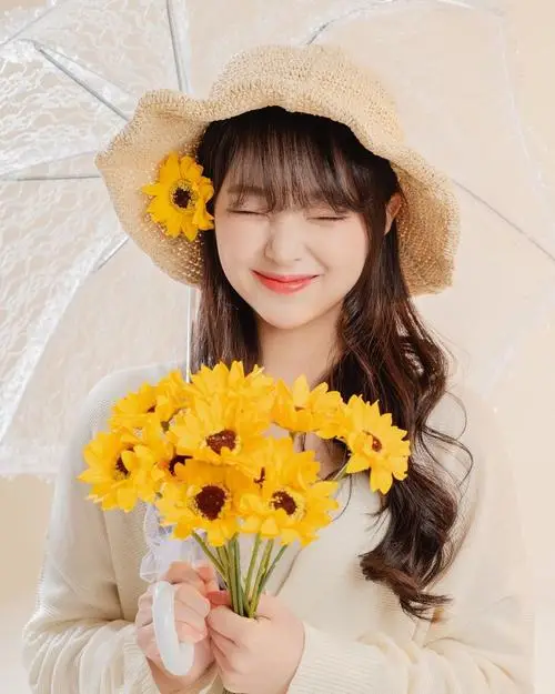 Hoa vàng che trước ngực, hình chân dung nữ đội nón cói mỉm cười khép mắt, áo sáng màu và nắng dịu